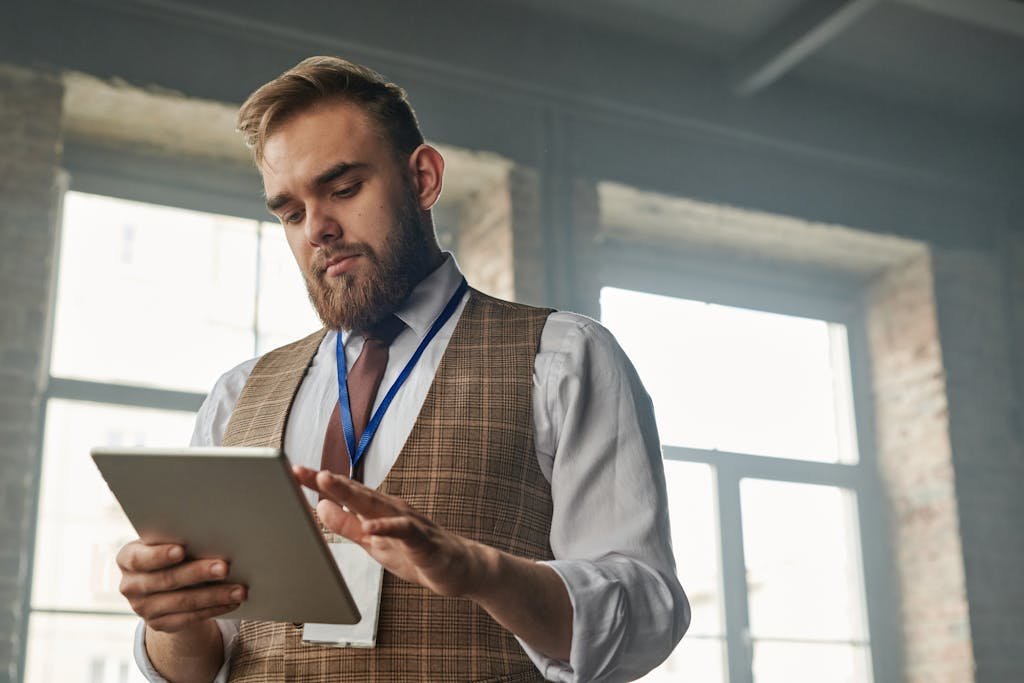 Businessman with a beard uses a tablet computer in a modern office setting, focusing on work.