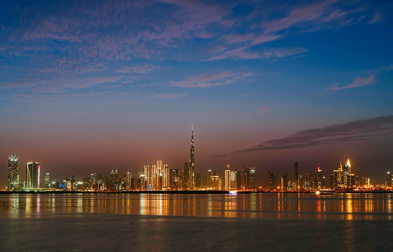 Scenic view of Dubai's skyline at twilight with the iconic Burj Khalifa illuminated across the waterfront.